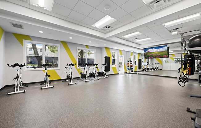 A gym with exercise bikes and a television screen.