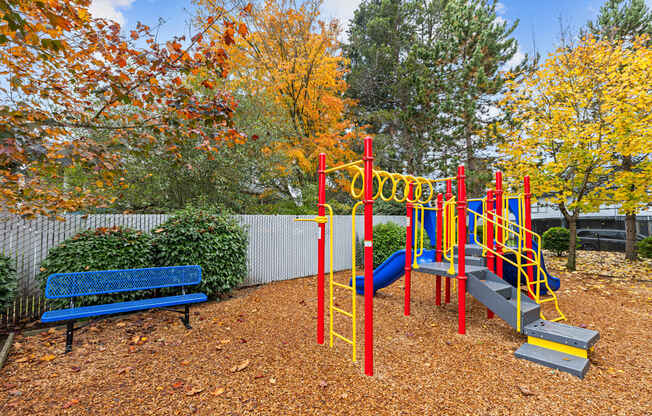 A playground with a red and yellow swing set and a blue bench.