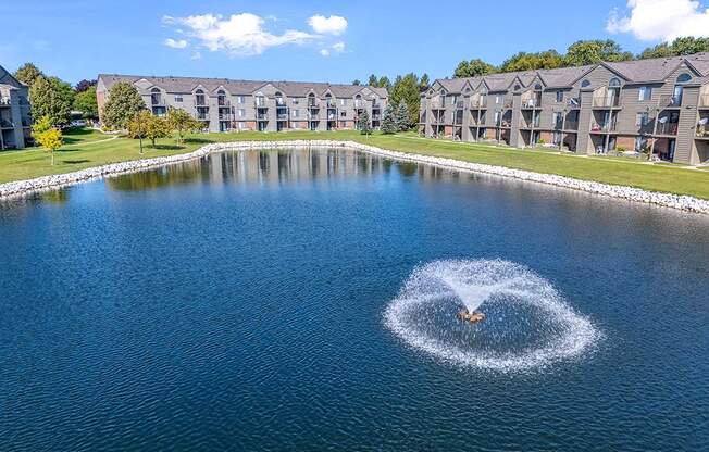 A fountain in the middle of a pond in back of apartment buildings at Oak Shores Apartments in Oak Creek, WI