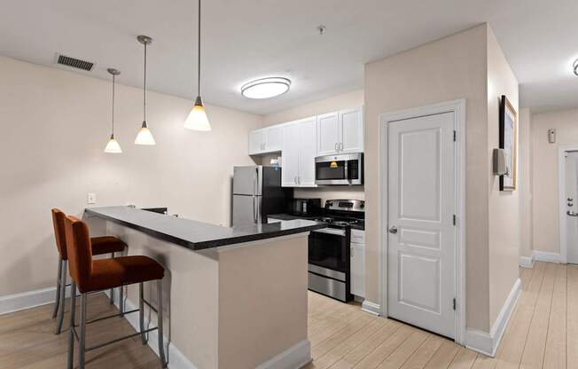 Ten05 West Trade's updated apartment featuring a black cut-down counter, stainless steel appliances including a refrigerator, oven and microwave, luxury vinyl tile flooring and hanging lights.