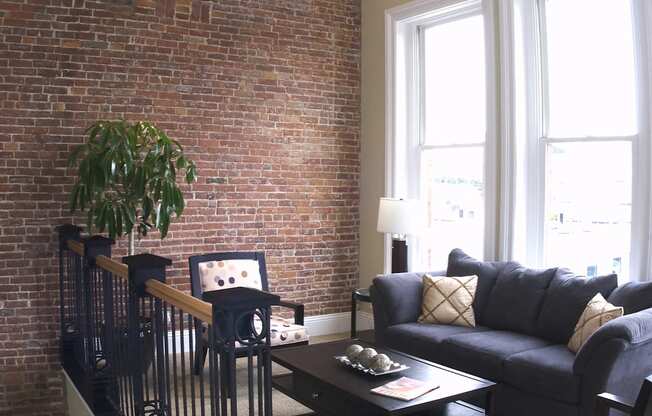 a living room with a brick wall and a couch and a table at The Granite Works Apartments , Buffalo, NY, 14202