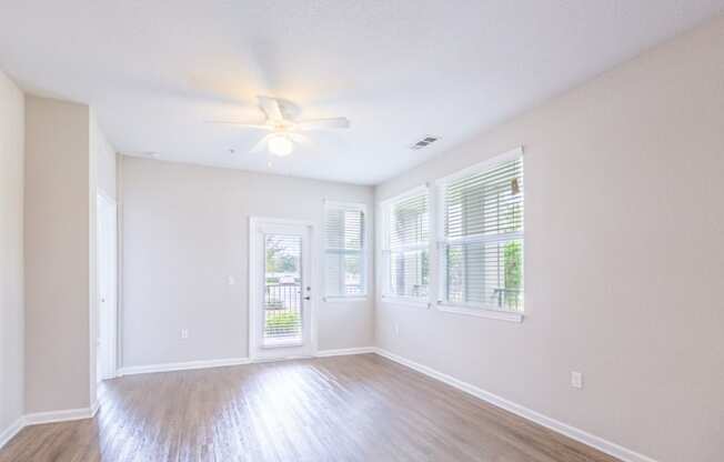 an empty living room with windows and a ceiling fan