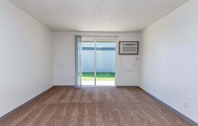 A room with a brown carpet and a sliding glass door leading to a backyard.