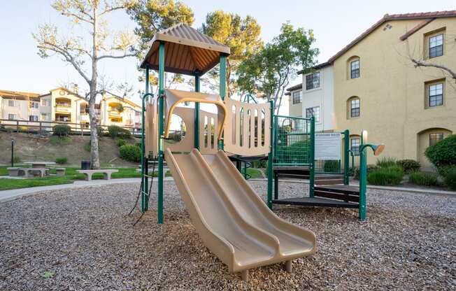 A playground with a slide and a green fence.
