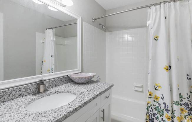 A bathroom with a floral shower curtain and a granite countertop.