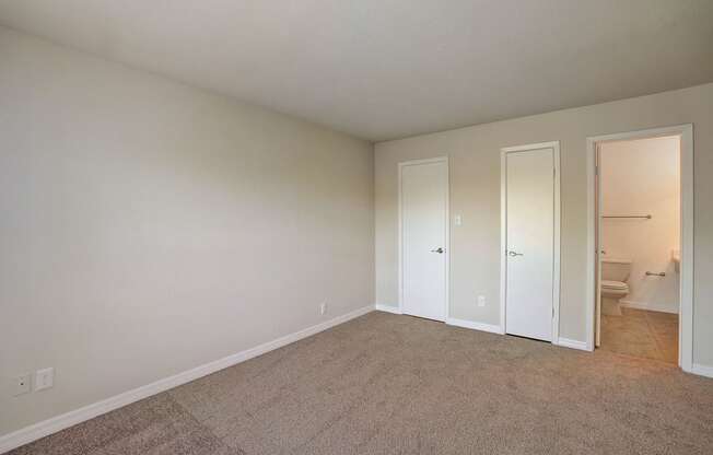 an empty living room with white walls and doors to a bathroom