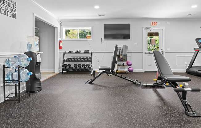 A gym room with a row of dumbbells and a bench.