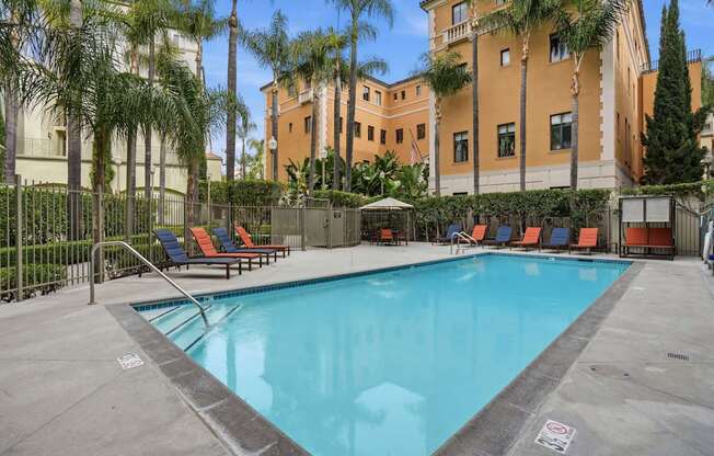 A pool surrounded by palm trees and lounge chairs.