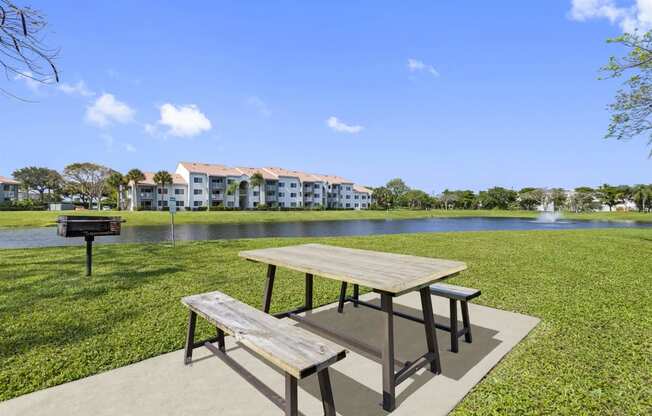 a picnic table in front of a lake with a grill