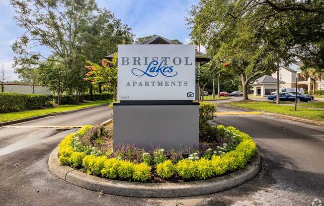 A sign for Bristol Lakes Apartments is surrounded by flowers and greenery.