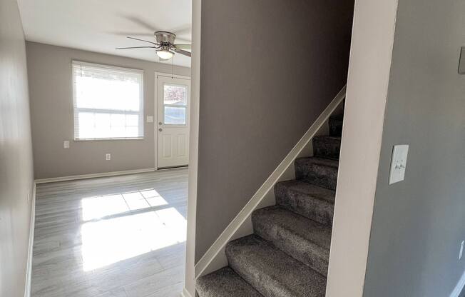 an empty living room with stairs and a ceiling fan