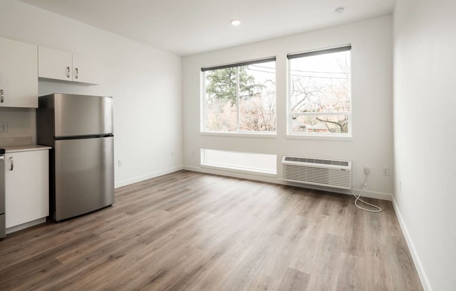 an empty living room with a refrigerator and a window