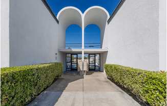 a walkway leading to the entrance of a white building with blue skiesat The Arches Apartments, LLC, El Cajon, CA