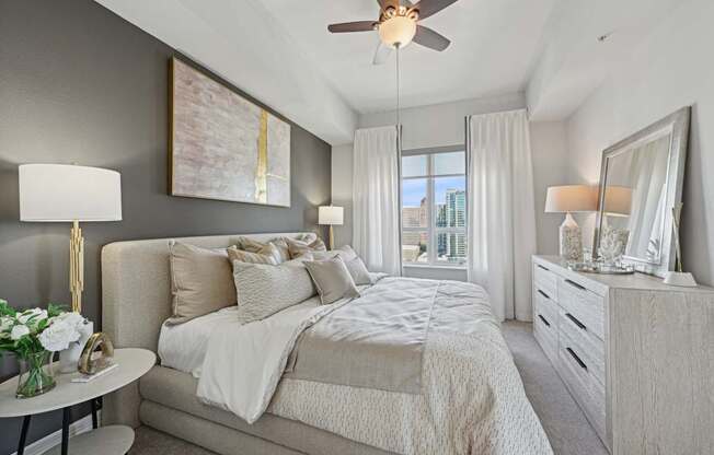 Model bedroom with a large bed, a ceiling fan, and a view of the city at Dominion Post Oak apartments in Houston, TX