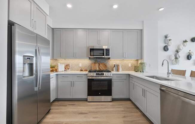 A modern kitchen with a stainless steel refrigerator and wooden flooring.