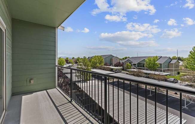 A balcony with a metal railing overlooks a street with cars and houses.
