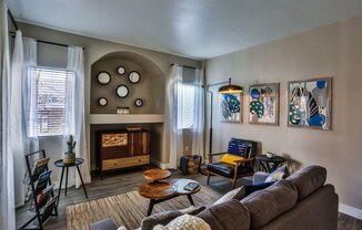 A living room with a grey couch, a wooden coffee table, and a fireplace with a mirror above it.