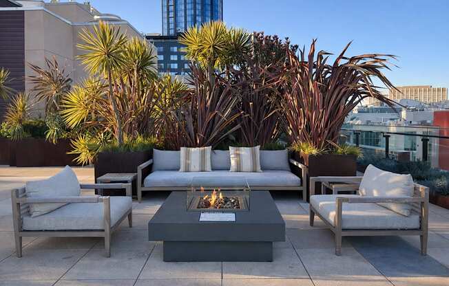A patio with a fire pit surrounded by chairs and cushions.