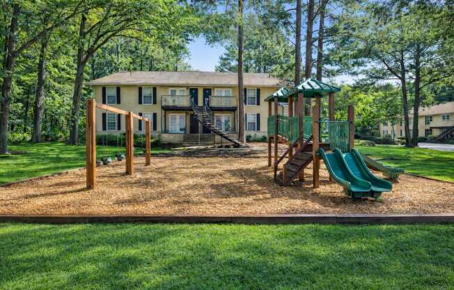 A playground with a green slide and a wooden swing set in front of a two-story house.