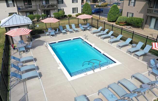 an aerial view of a pool with chairs and umbrellas and an apartment building