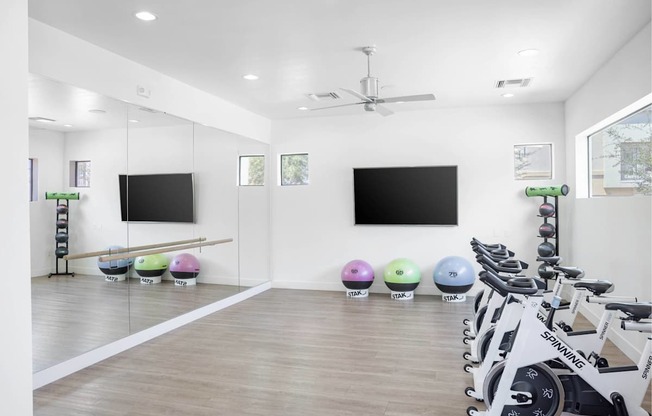 A gym with a row of exercise bikes and two television screens on the wall.