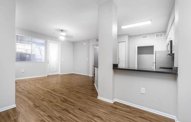 A spacious living room with hardwood floors and a kitchenette in the background.