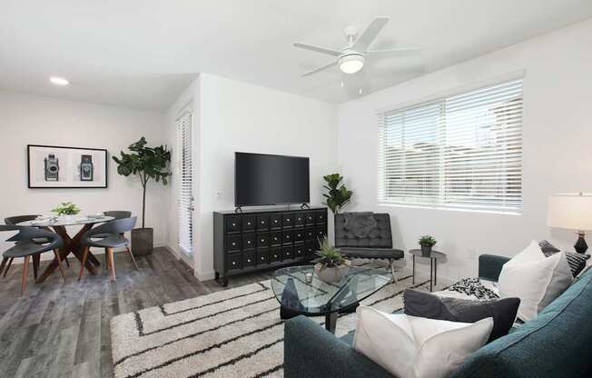 A living room with a grey couch, a glass table, a television, and a ceiling fan.