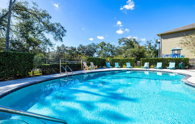 A large outdoor swimming pool surrounded by trees and lounge chairs.