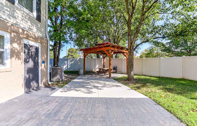 A wooden gazebo is situated in a backyard with a paved walkway leading to it.