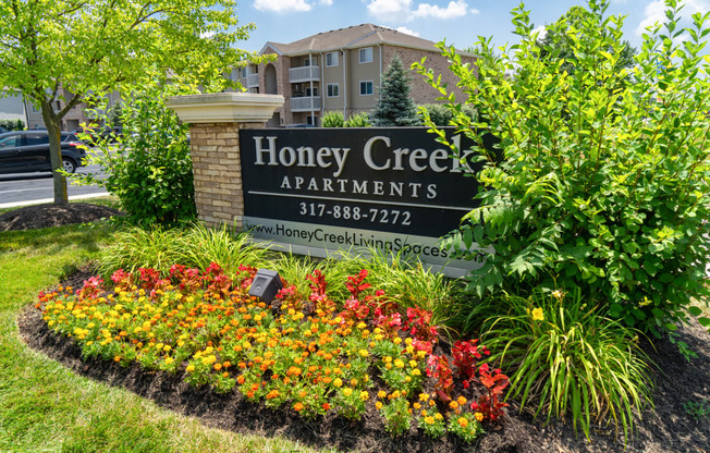 a sign for honey creek apartments in front of a flower garden