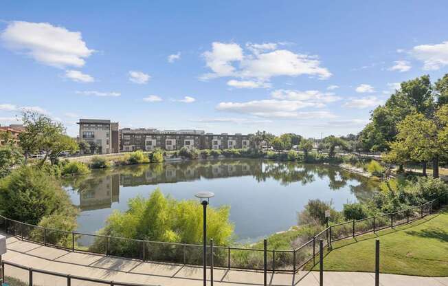 A serene park with a lake, trees, and a building in the background.