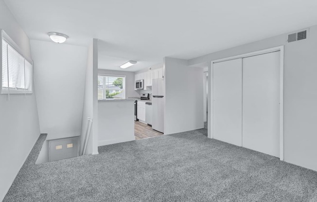 the living room and kitchen of an apartment with white walls and carpet