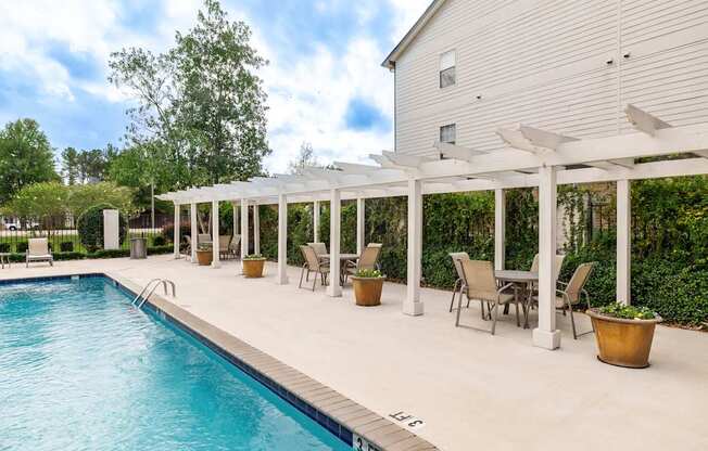 A pool with a white pergola and chairs around it.