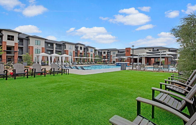 49 West's modern apartment complex with a pool area, surrounded by lush grass and chairs. Bright, sunny day with scattered clouds, creating a serene atmosphere.