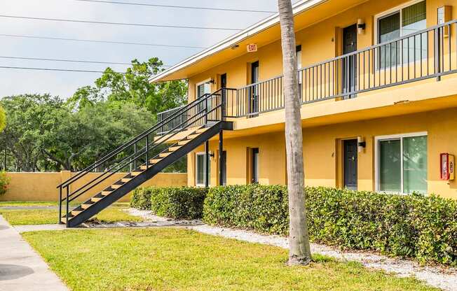 a yellow house with a staircase and a grass yard