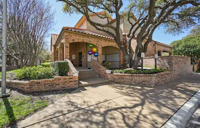 A house with a brick wall and a tree in front.