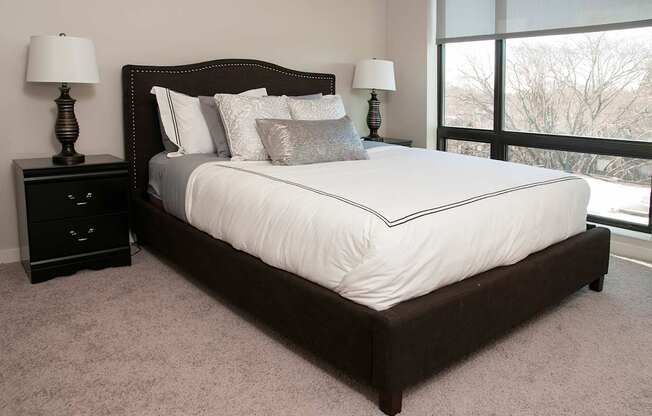 A bed with a white sheet and pillows is in a room with a carpet and two lamps.