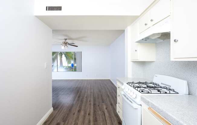 an empty kitchen and living room with white appliances and a ceiling fan