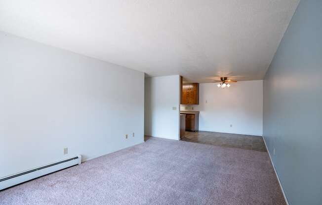 the living room and dining room of an apartment with carpet and white walls. Fargo, ND Betty Ann Apartments