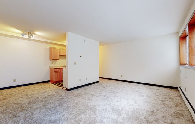 a bedroom with a white wall and a white door with a kitchen in the background