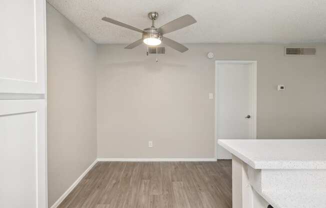 an empty living room with a ceiling fan and a kitchen