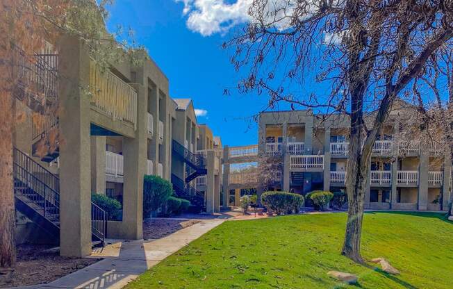 a row of apartment buildings with a green lawn and trees