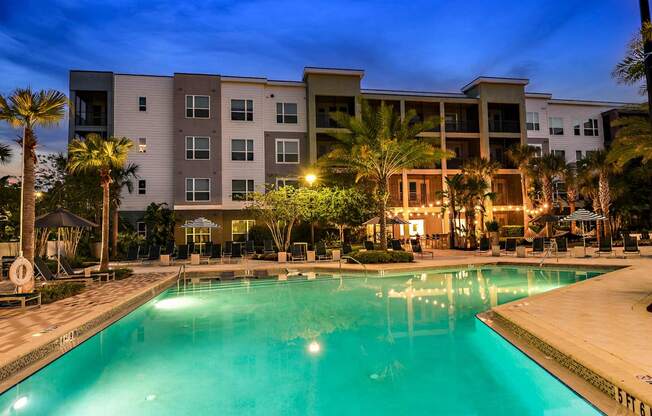 a large swimming pool in front of an apartment building at night