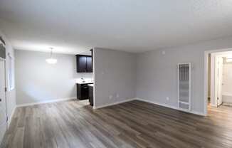 an empty living room with wood flooring and a kitchen