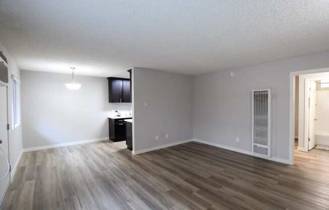 an empty living room with wood flooring and a kitchen