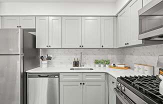 A modern kitchen with a stainless steel refrigerator, a white countertop, and a black stove top.