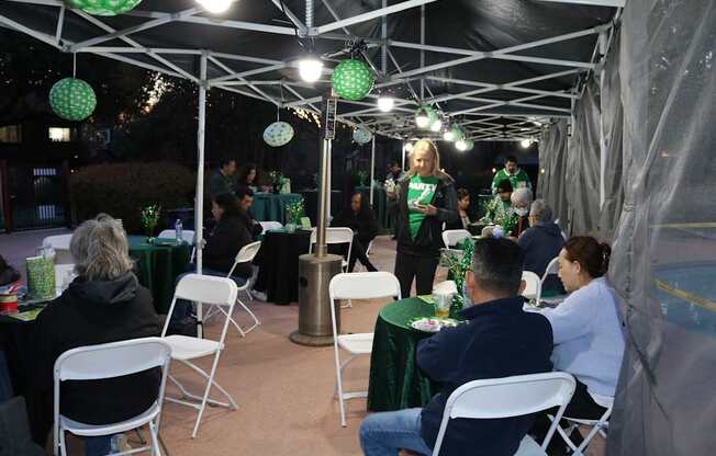 A group of people are gathered under a tent with green and white decorations.