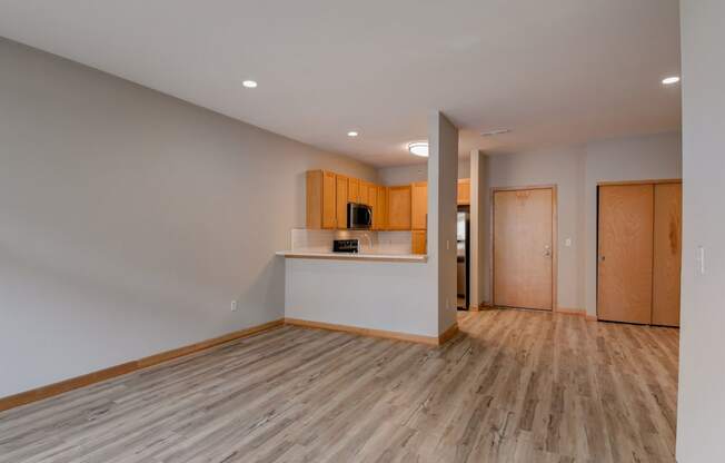an empty living room with wood flooring and a kitchen