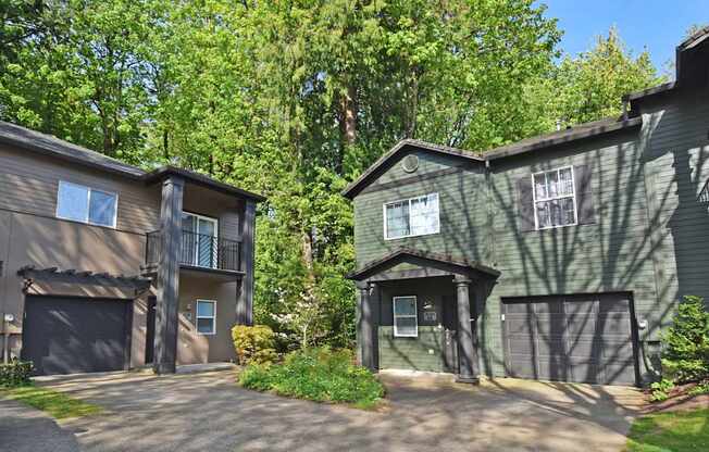 Two houses with garages are surrounded by trees.
