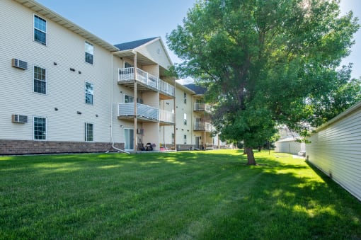 a large grassy area with a tree in front of an apartment building